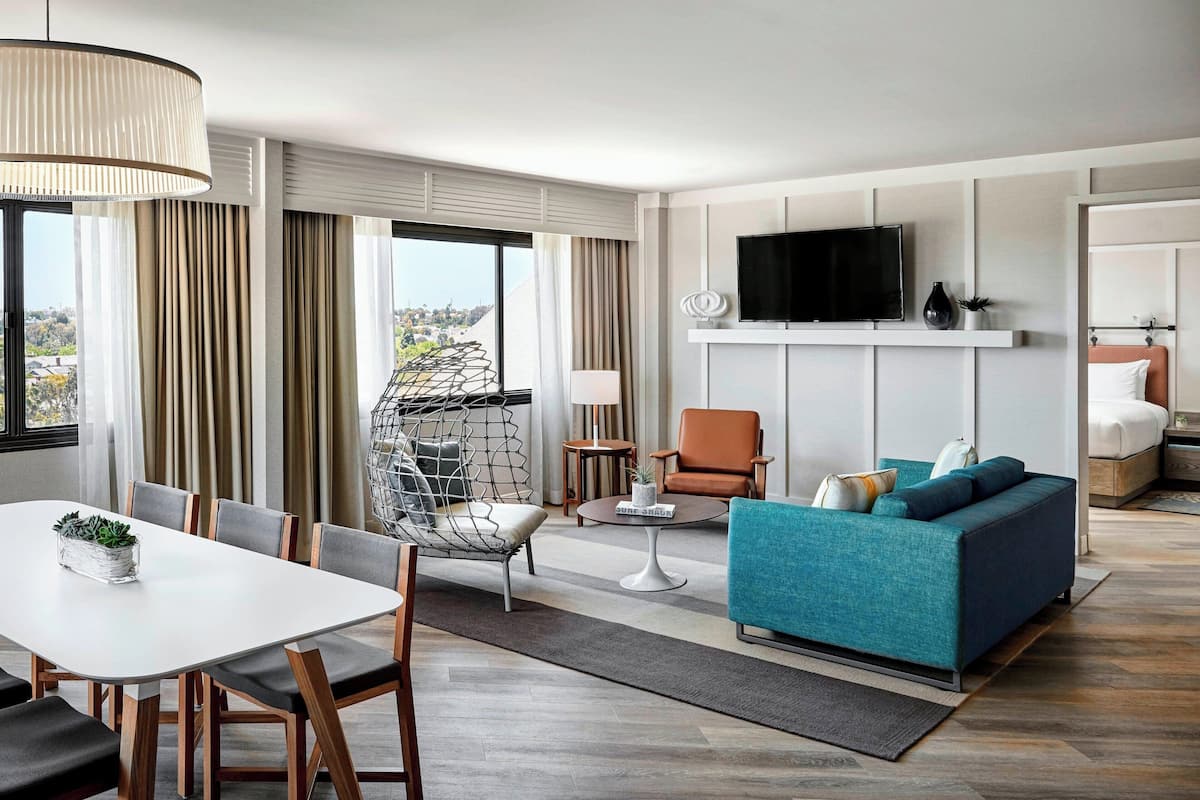 A modern hotel room with a dining area, a sofa, a TV, and a bed.