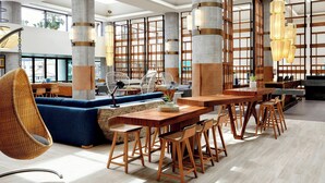 A modern interior with high ceilings, large windows, and a mix of seating areas including a blue sofa and wooden tables with chairs. - Westdrift Manhattan Beach, Autograph Collection by Marriott (Manhattan Beach)