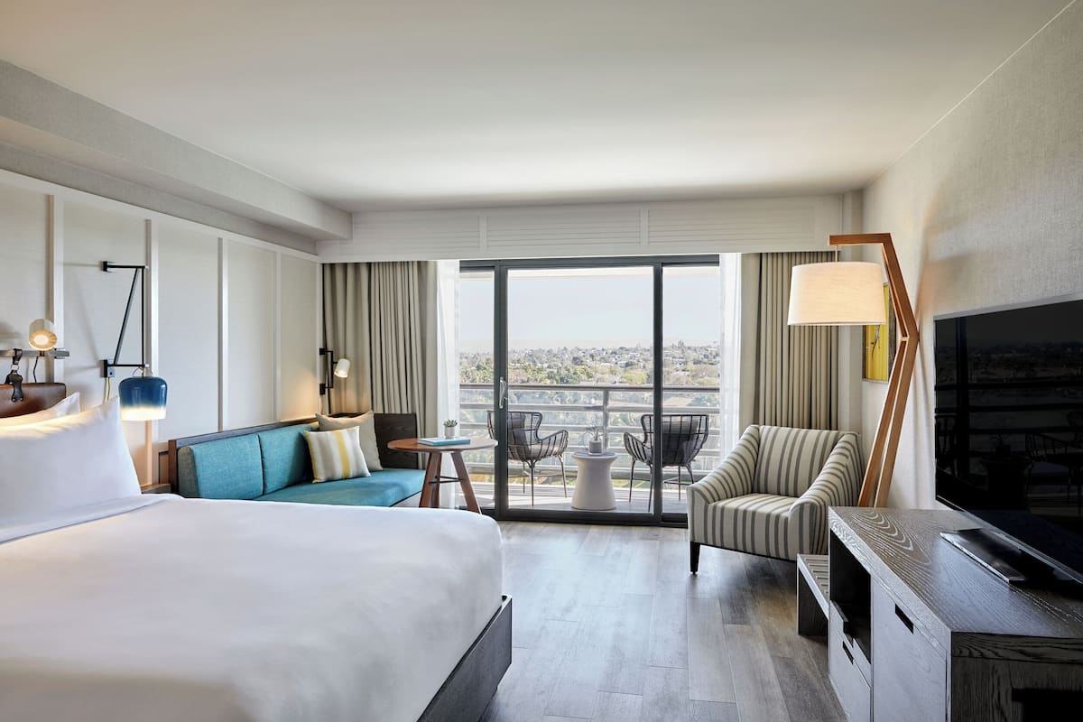 A hotel room with a bed, a sofa, a TV, a desk, and a balcony with a view.