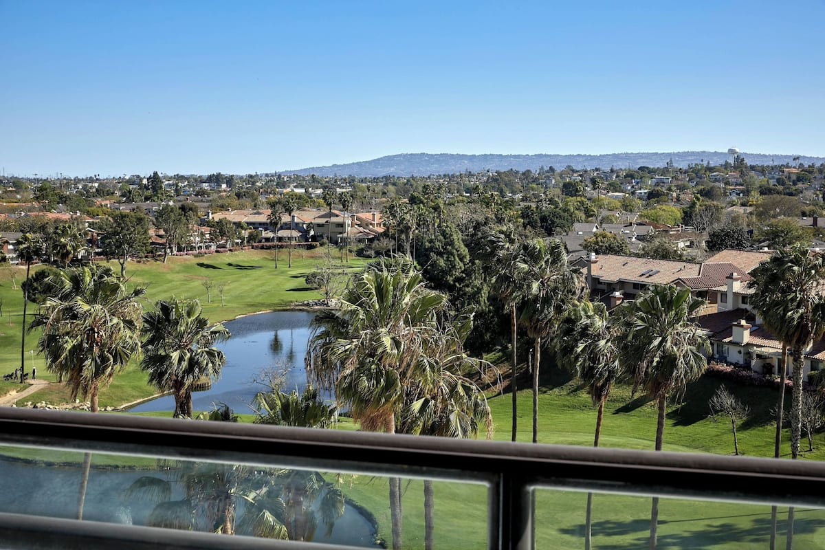 A residential area with a golf course, a pond, and houses with a mountain in the background.