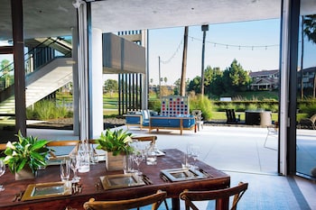 A modern interior with high ceilings, large windows, and a mix of seating areas including a blue sofa and wooden tables with chairs. at Westdrift Manhattan Beach, Autograph Collection by Marriott