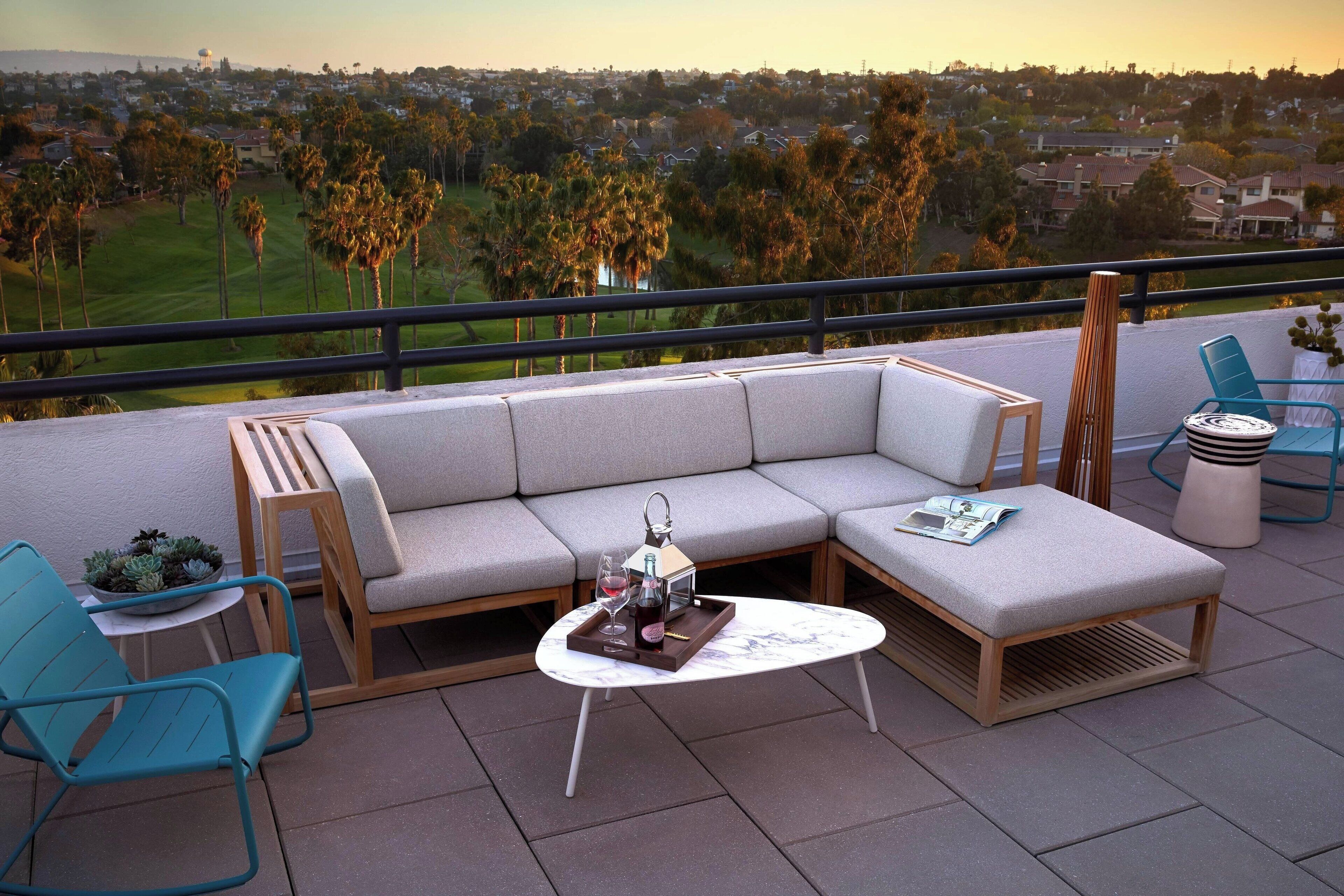 Un balcón con un sofá modular, dos sillones, una mesita con bandeja, y vistas a un campo de golf y una zona residencial.