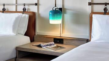 Et hotelværelse med to senge, et natbord med et magasin, og en lampe monteret på væggen.
