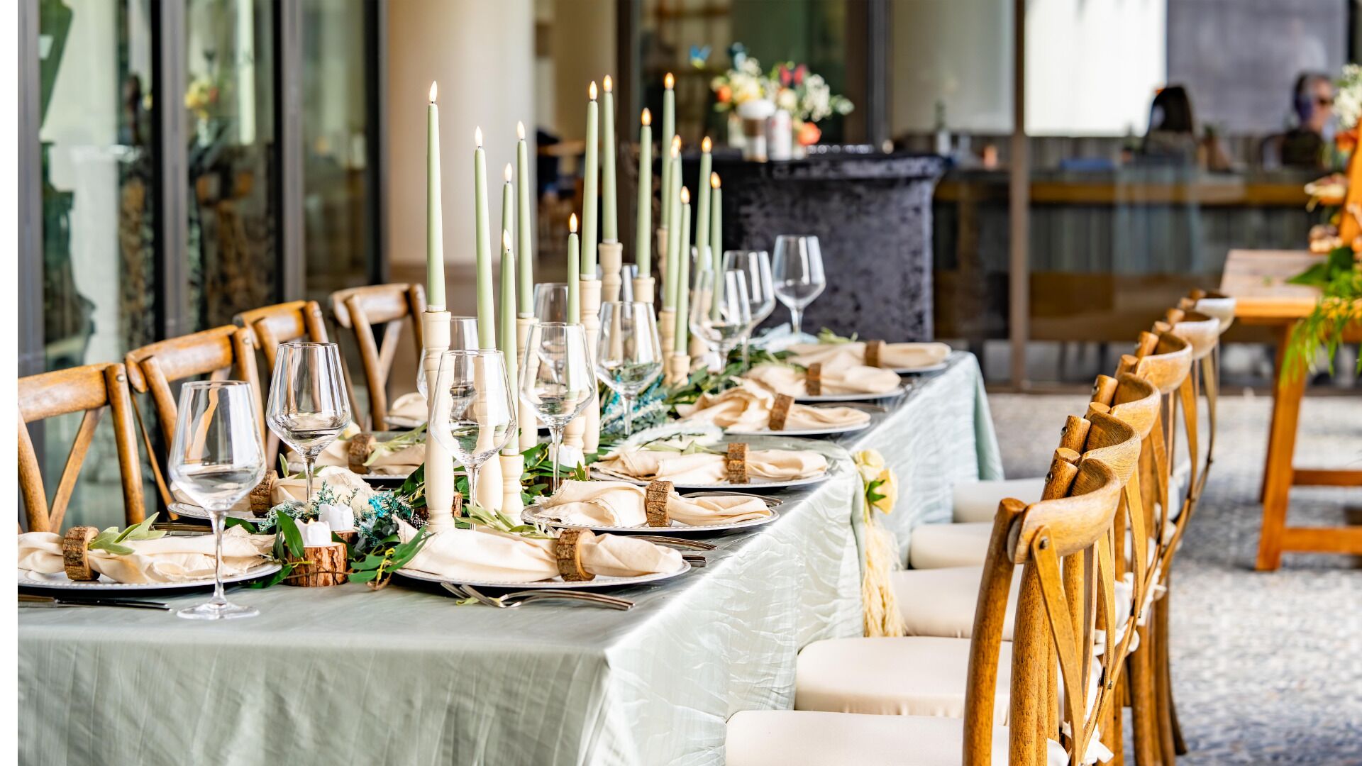 A long dining table set with candles, wine glasses, and plates, surrounded by wooden chairs.