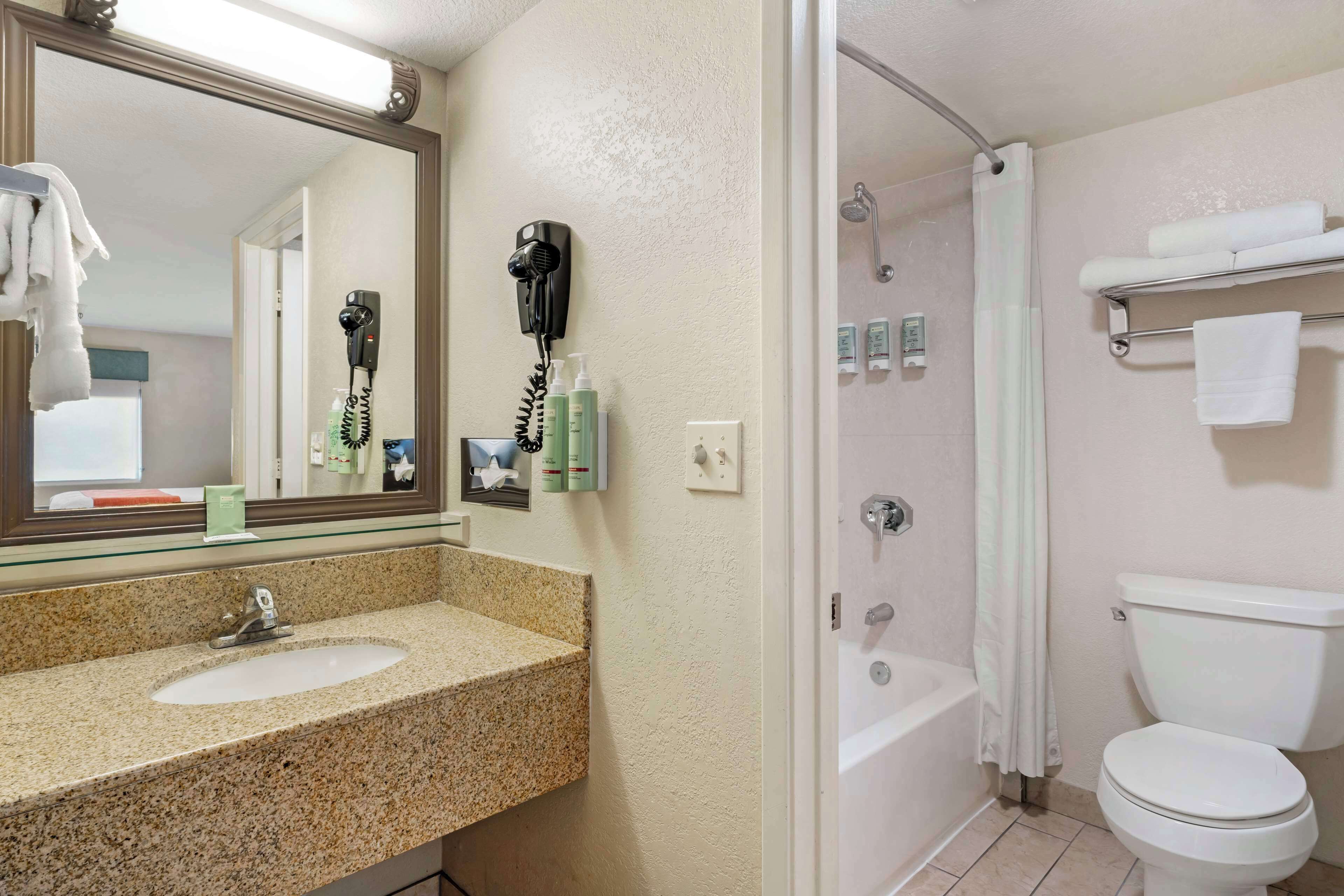 Une salle de bain avec un lavabo doté d’un plan de travail en granit, un miroir, un sèche-cheveux et un espace douche.