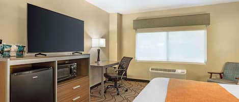 Habitación de hotel con cama, escritorio con computadora, microondas, refrigerador, televisor, silla y ventana con vistas.