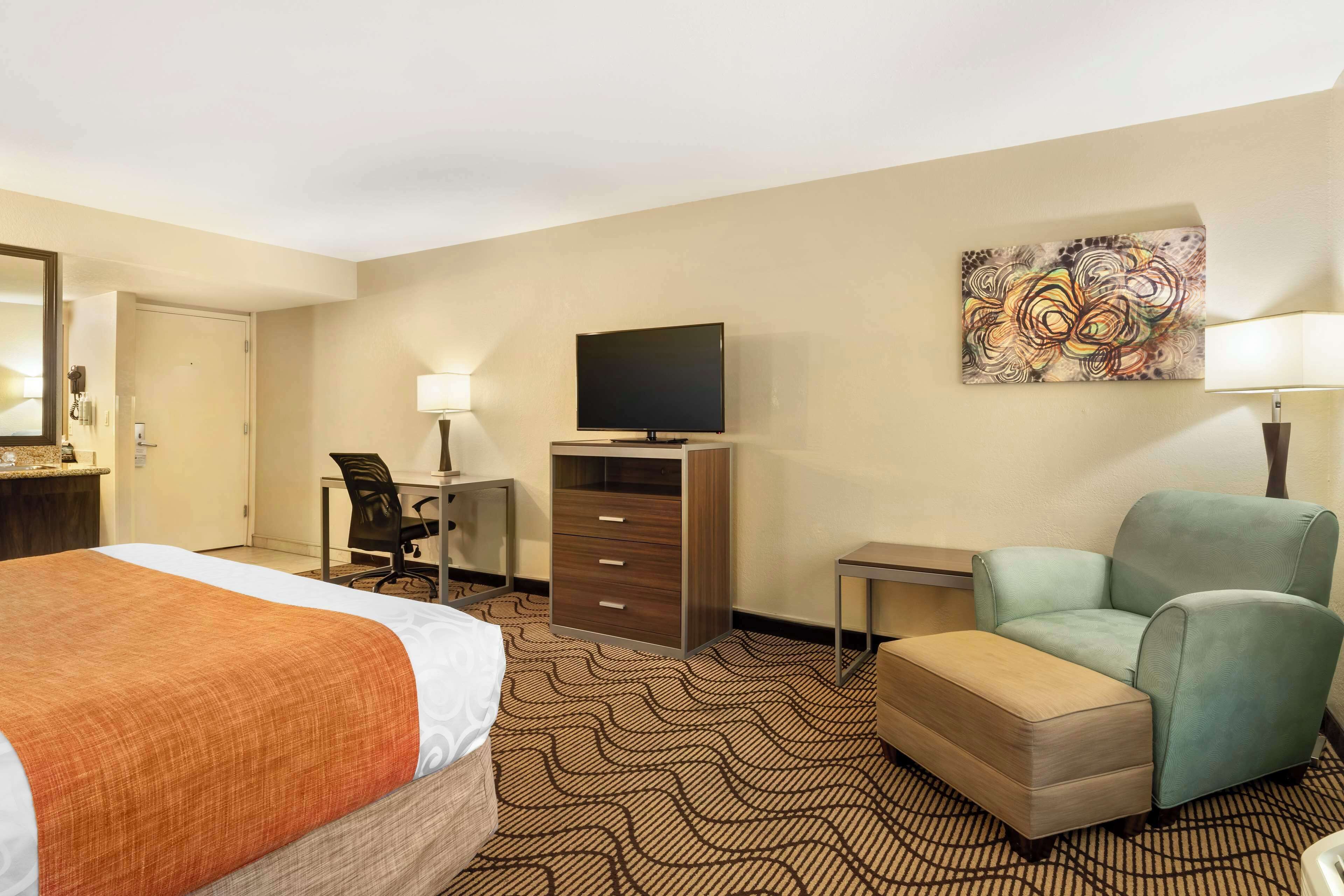 Ein Hotelzimmer mit Bett, Schreibtisch mit Stuhl, Fernseher, Sofa und einem Gemälde an der Wand.