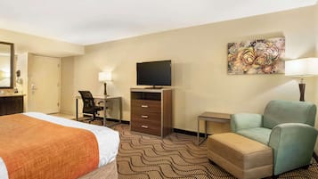 A hotel room with a bed, a desk with a chair, a television, a sofa, and a painting on the wall.