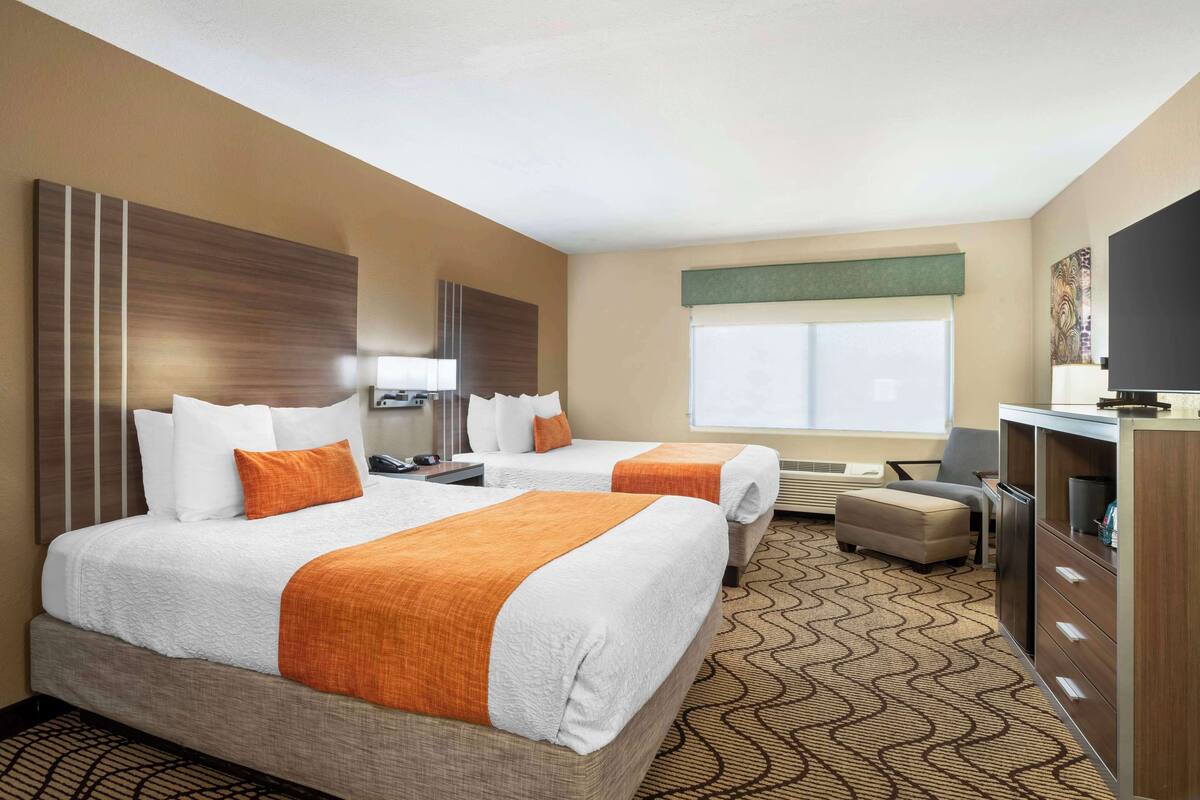 A hotel room with two beds, a desk, a TV, and a large window.