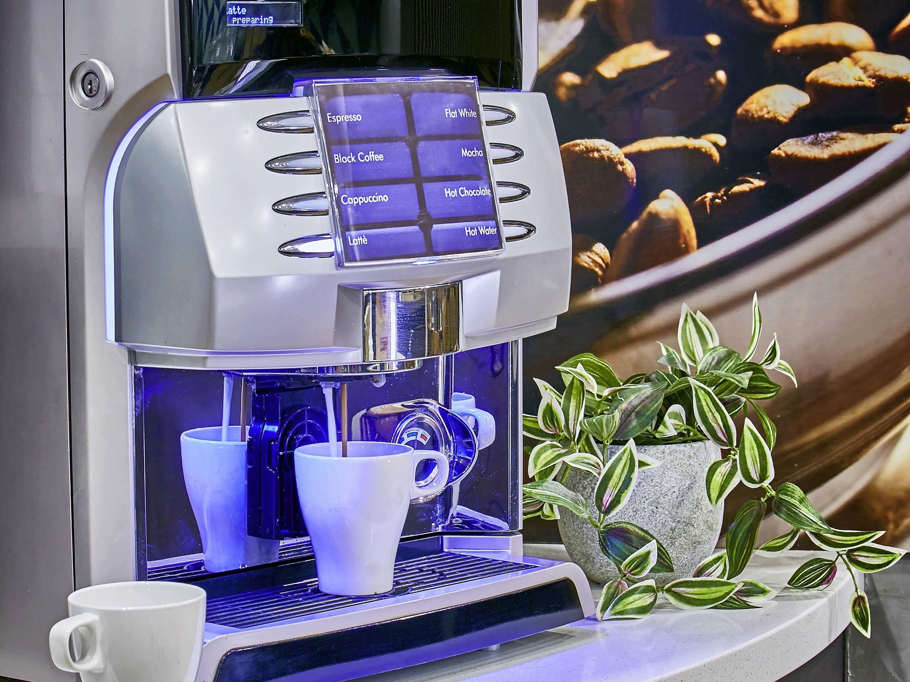 A coffee machine with a selection panel and two cups below it.