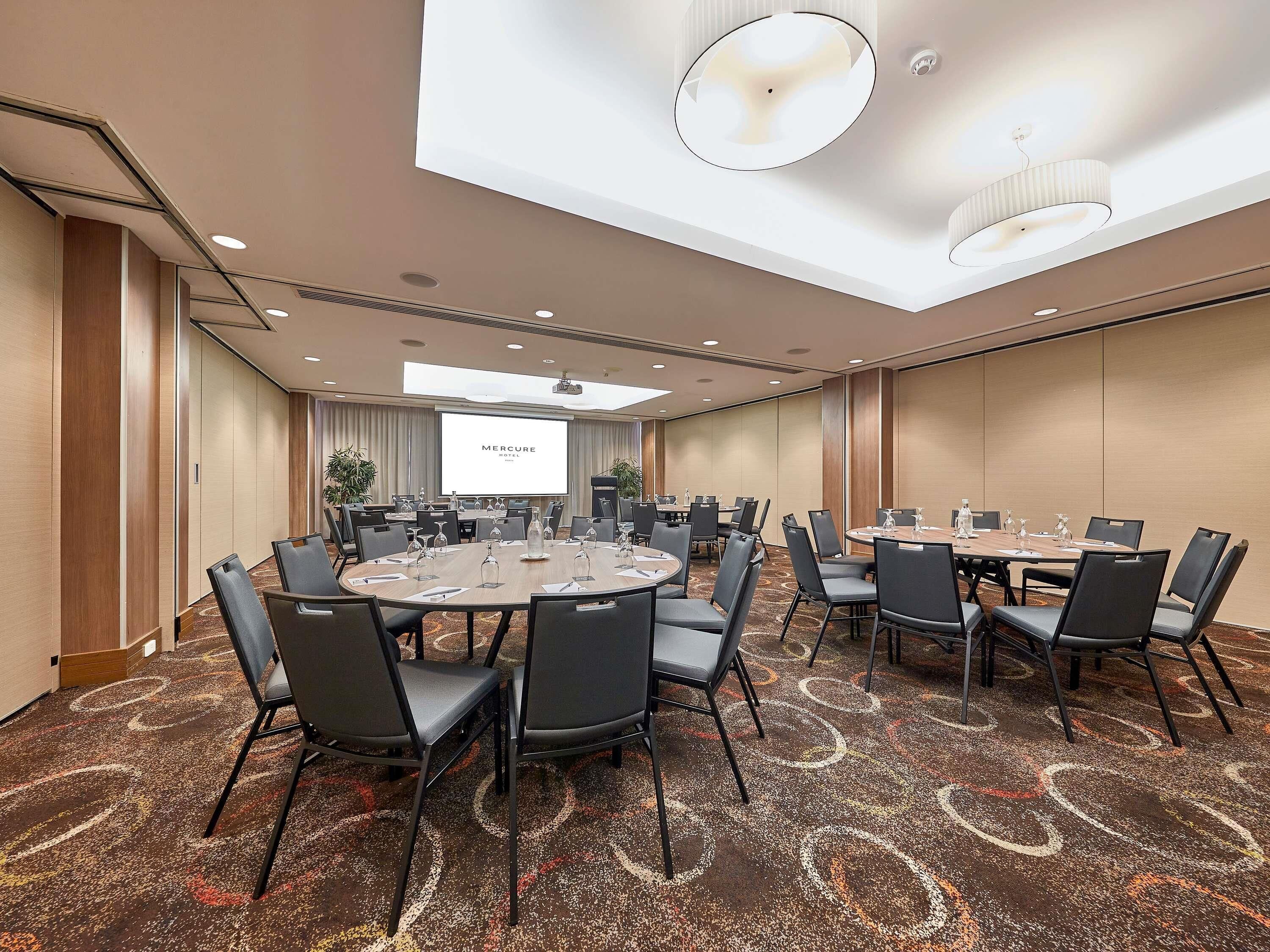 A conference room with round tables, chairs, a projector screen, and a carpeted floor.