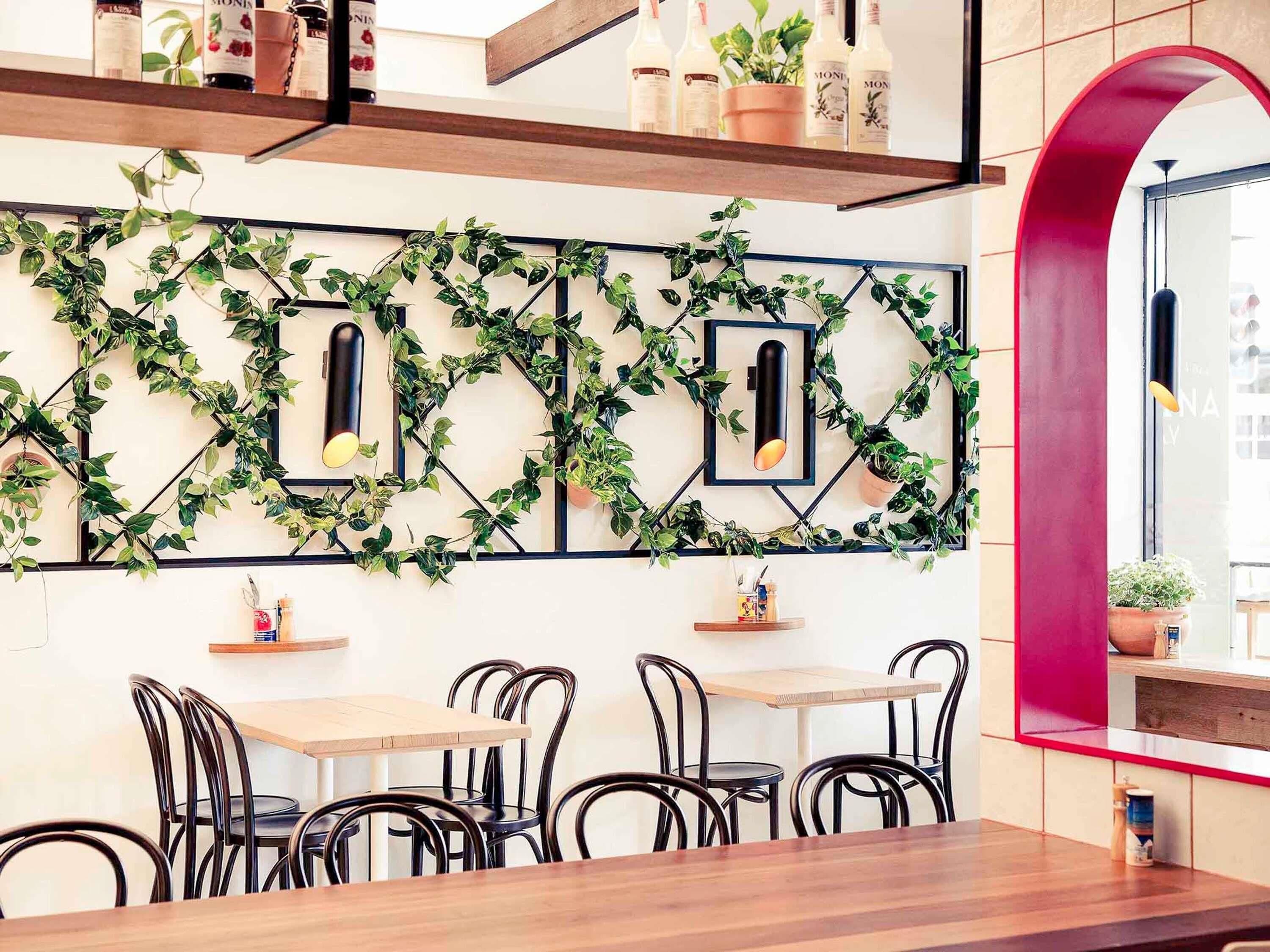 A restaurant interior with a modern design, featuring a wall-mounted plant display, wooden tables, and black metal chairs.