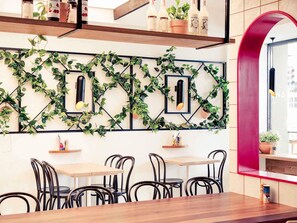 A restaurant interior with a modern design, featuring a wall-mounted plant display, wooden tables, and black metal chairs.