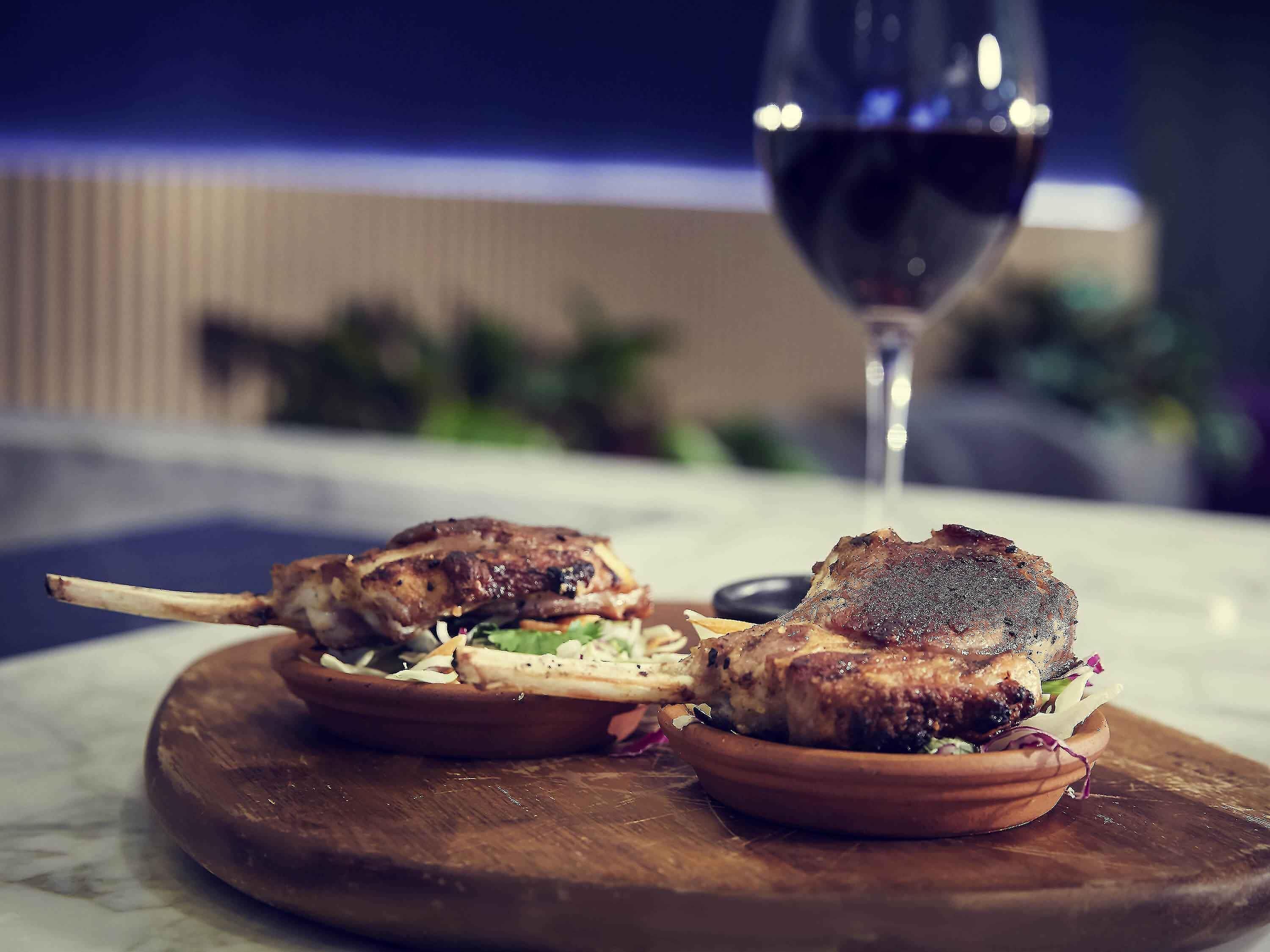 Une assiette avec deux plats de viande grillée, présentée sur une planche en bois, un verre de vin rouge et un arrière-plan flou.