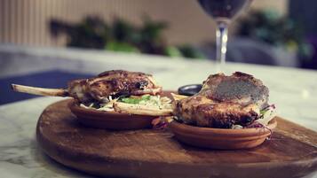 Une assiette avec deux plats de viande grillée, présentée sur une planche en bois, un verre de vin rouge et un arrière-plan flou.