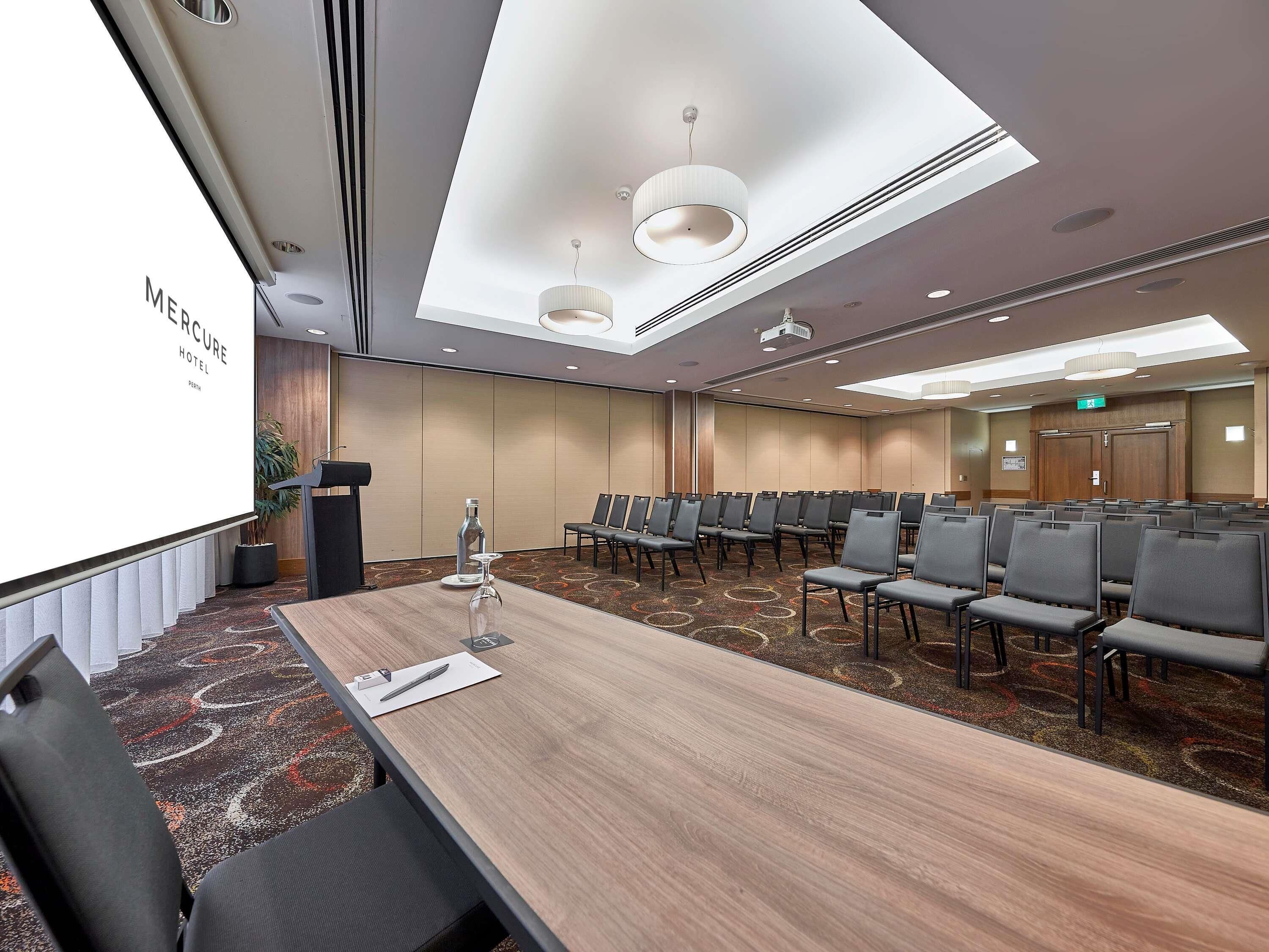 A conference room with a long table, chairs, a projector screen, and a carpeted floor.