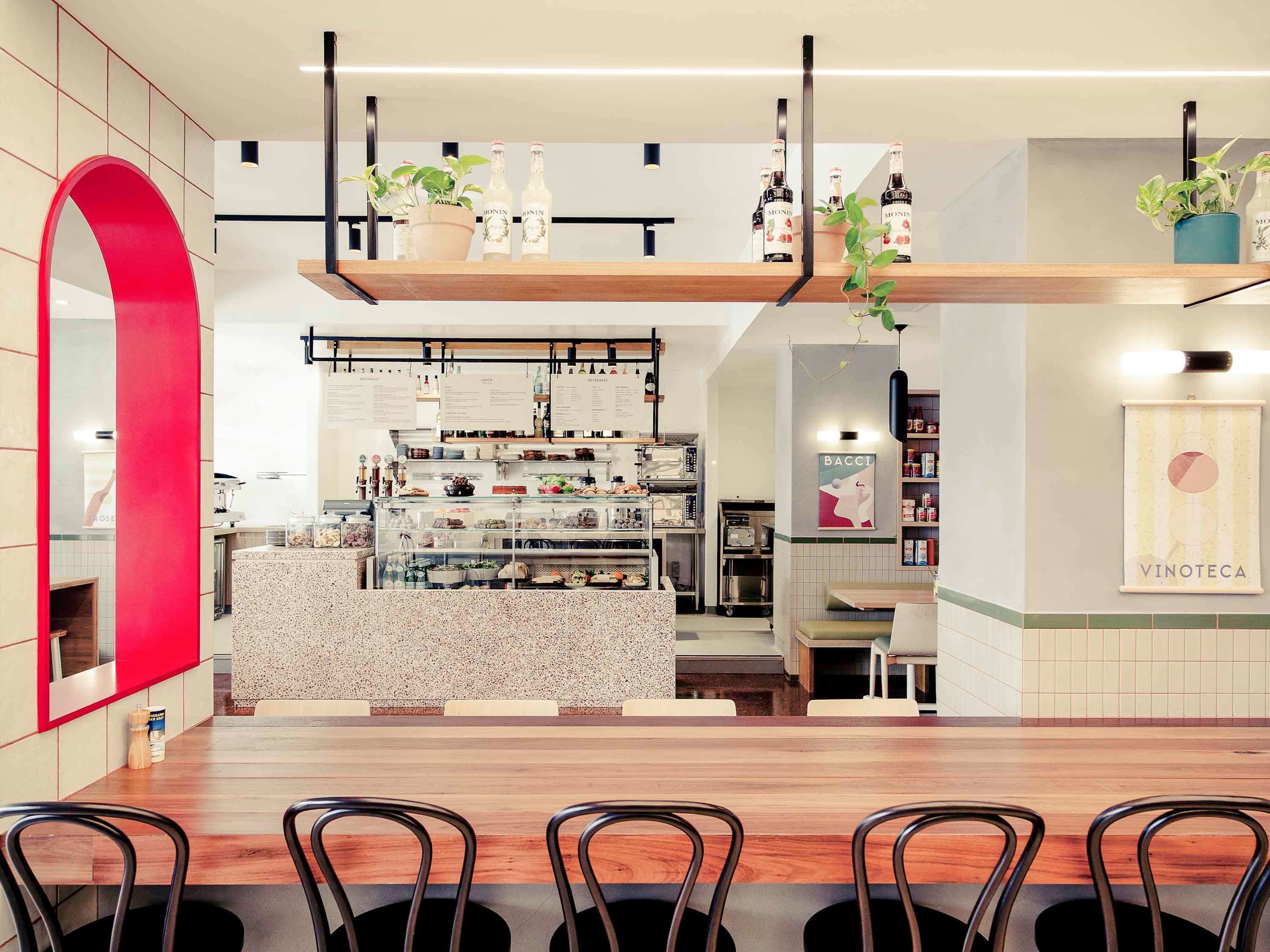 A modern restaurant interior with a wooden dining area, a counter with food displays, and a bar area with shelves and potted plants.