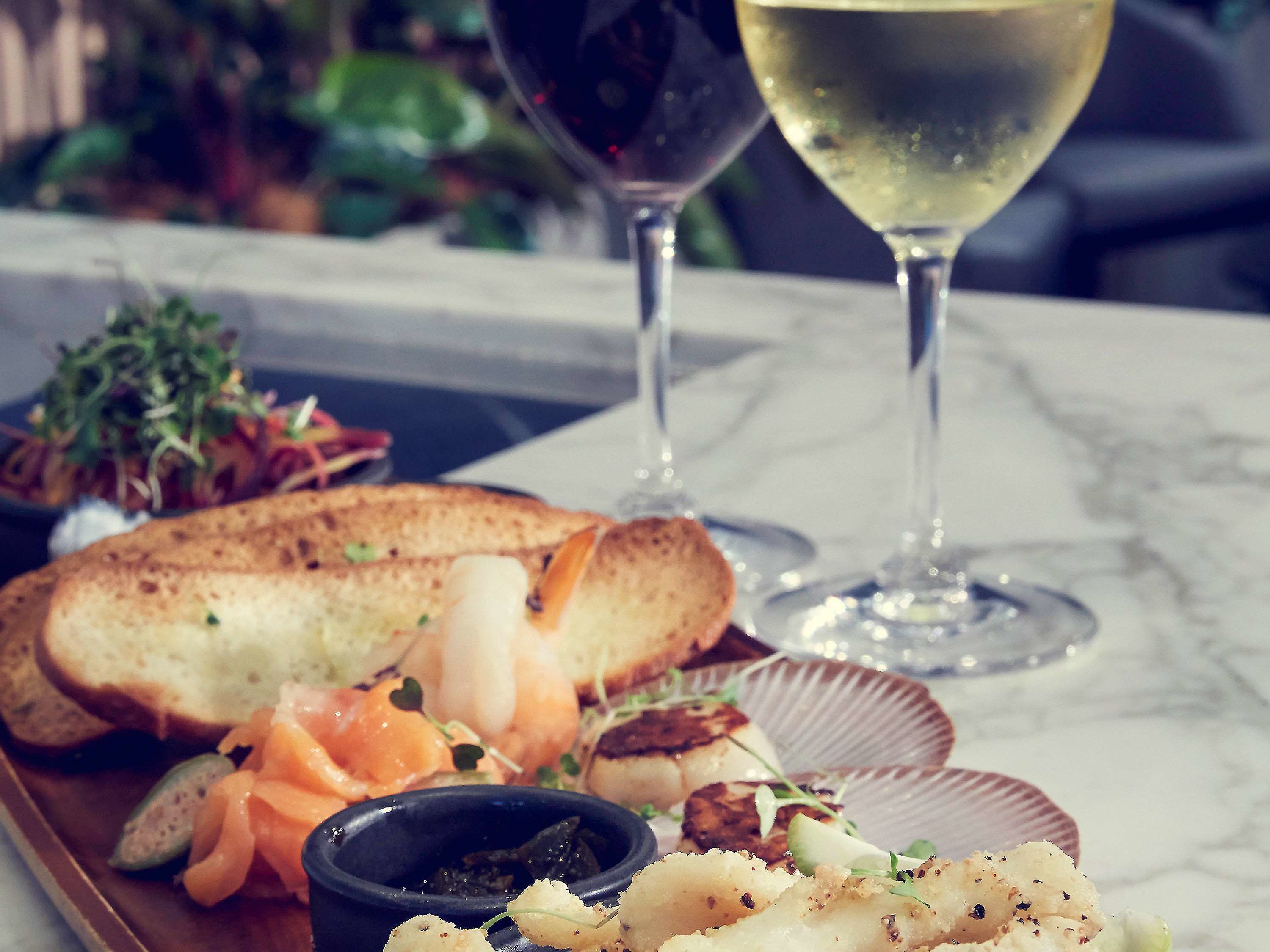 A dining table with a plate of food, including bread, salmon, and a small bowl of sauce. Two wine glasses are also visible.