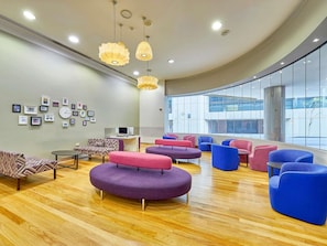 A modern lounge area with round seating, a computer desk, and a large window offering a view of the outside.