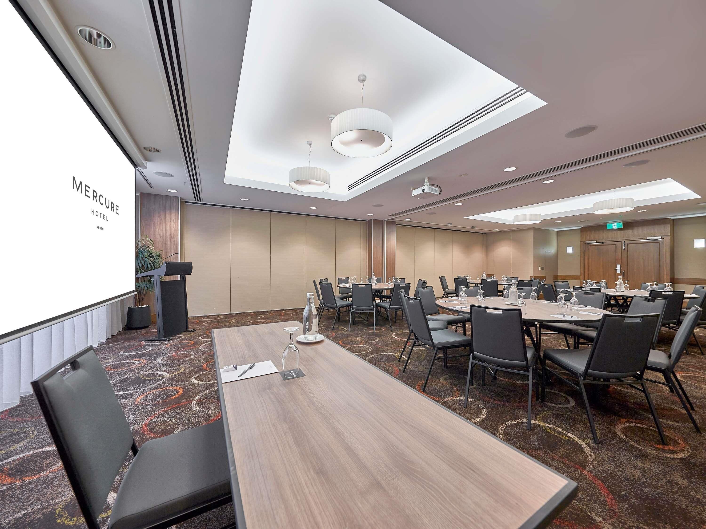 Un salón de conferencias con una gran mesa, sillas, una pantalla de proyector y un orador.