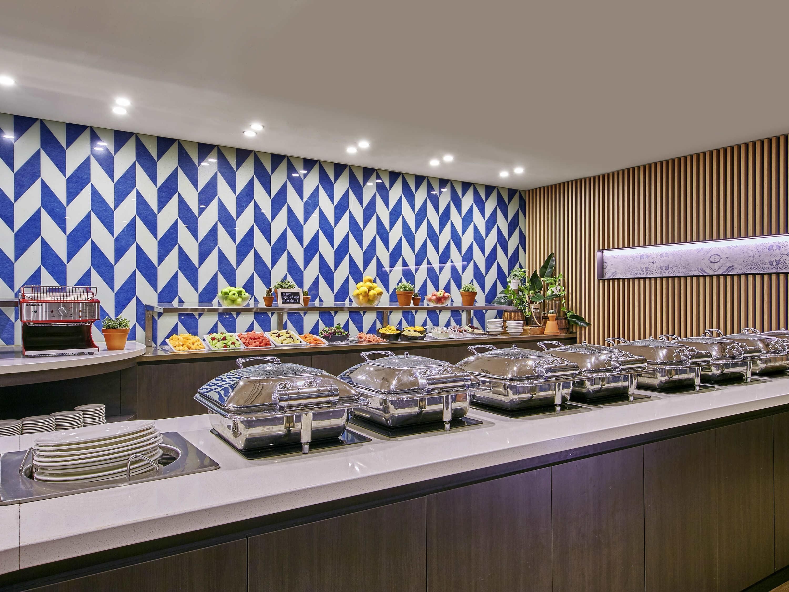 Montaje de bufé con una pared de diseño azul y blanco, una parrilla y diversos alimentos.