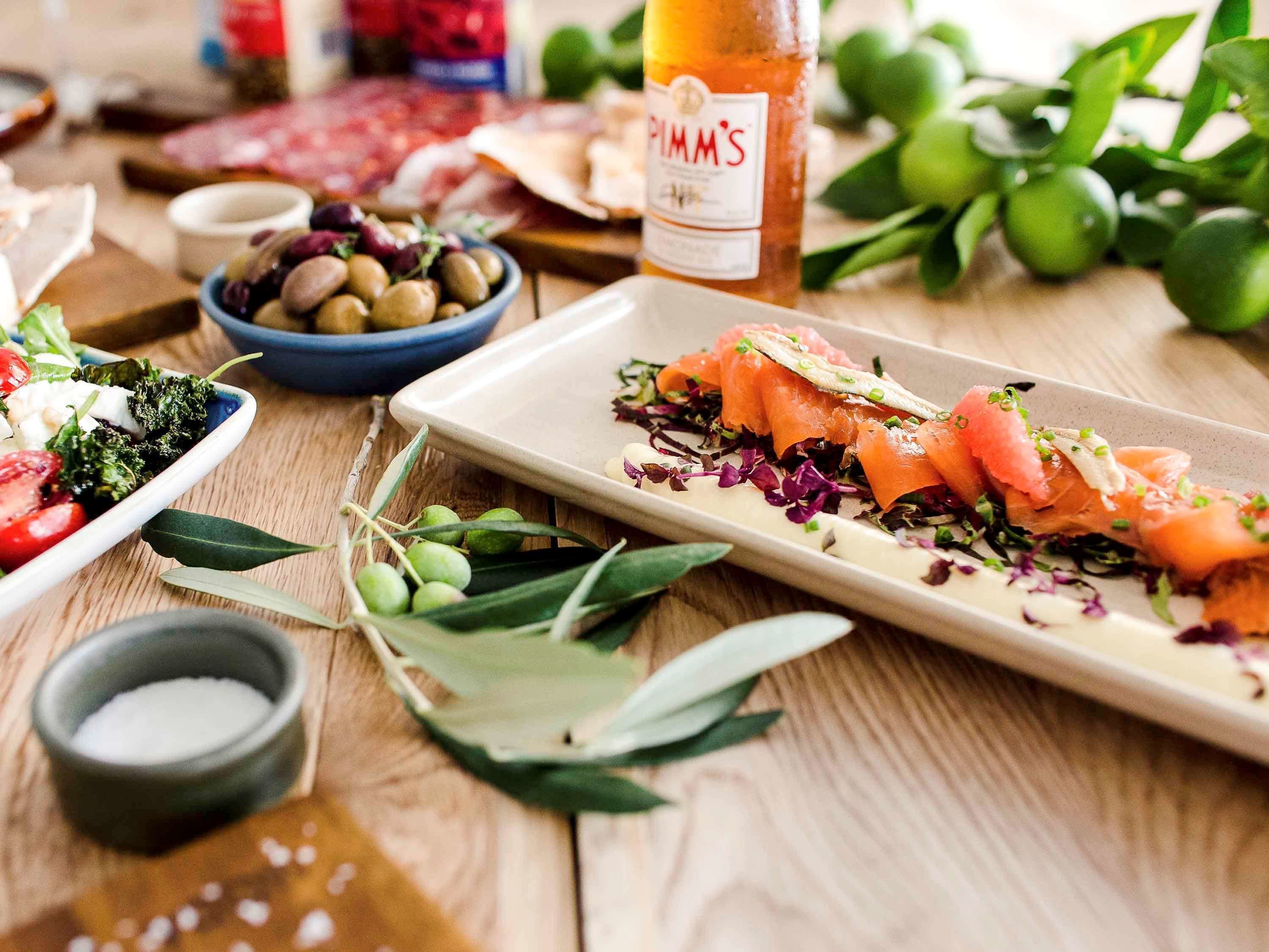 Ein Holztisch mit verschiedenen Speisen, darunter Lachs, Oliven und Salat.