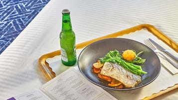 Un plateau repas comprenant un plat de poisson, des légumes et une bouteille verte, accompagné d’un menu.