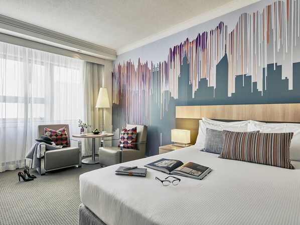 A hotel room with a large bed, two armchairs, a small table, and a cityscape mural on the wall. - Mercure Perth (Perth)