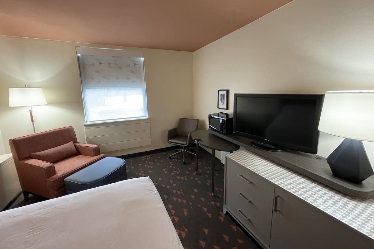 A hotel room with a bed, a desk, a television, a chair, and a lamp.