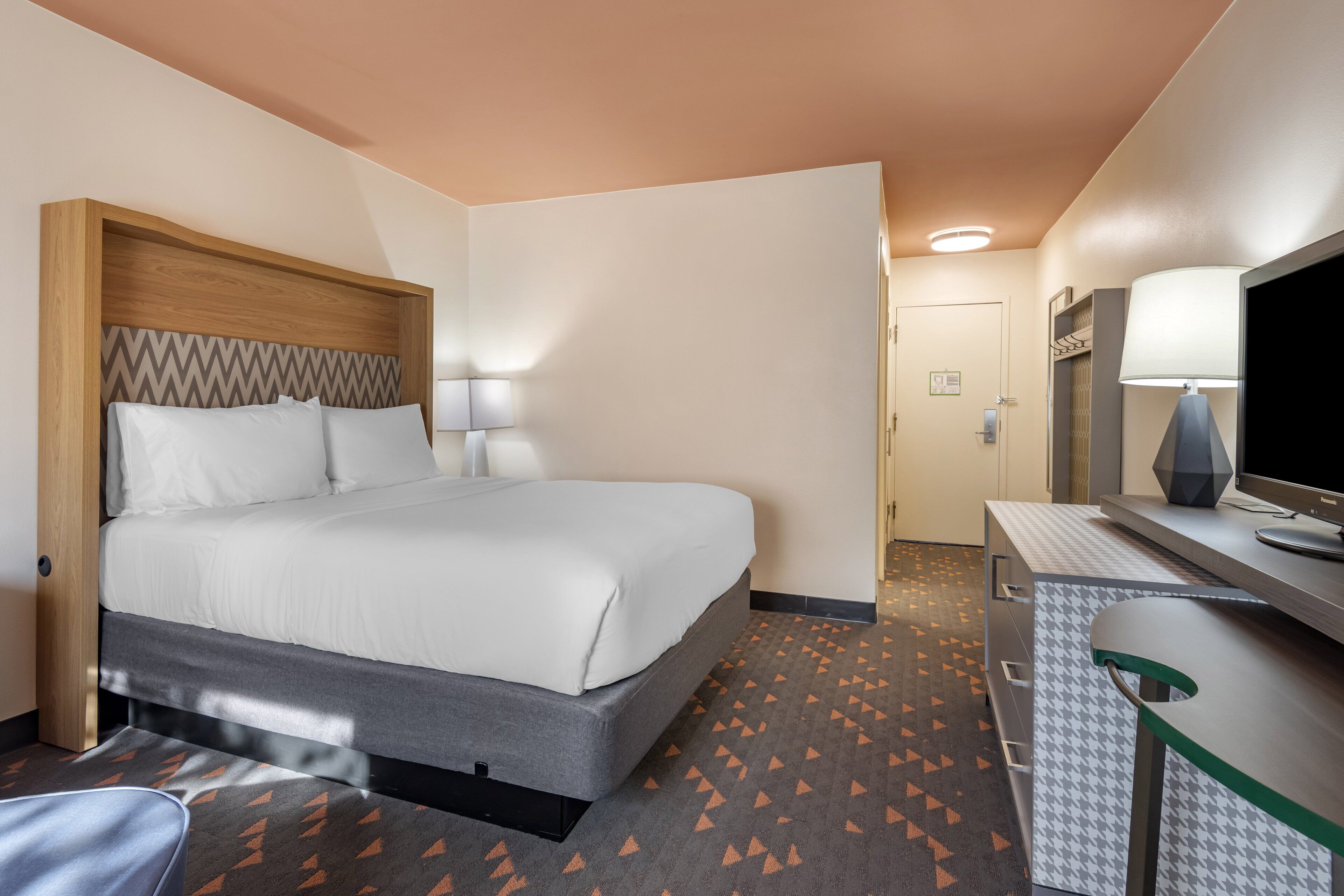 Quarto de hotel com cama, escrivaninha, televisão e porta que dá para outro quarto.