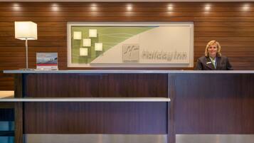 Un mostrador de recepción con diseño de paneles de madera, un cartel enmarcado con el nombre 'Holiday Inn' y una lámpara a la izquierda.