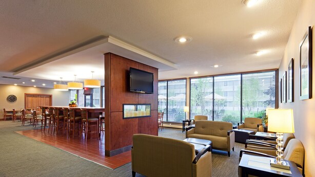 A hotel lobby with a dining area, seating, a TV, and large windows.
