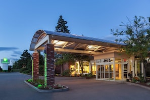 A Holiday Inn hotel entrance with a covered waiting area, brick pillars, and a glass entrance.