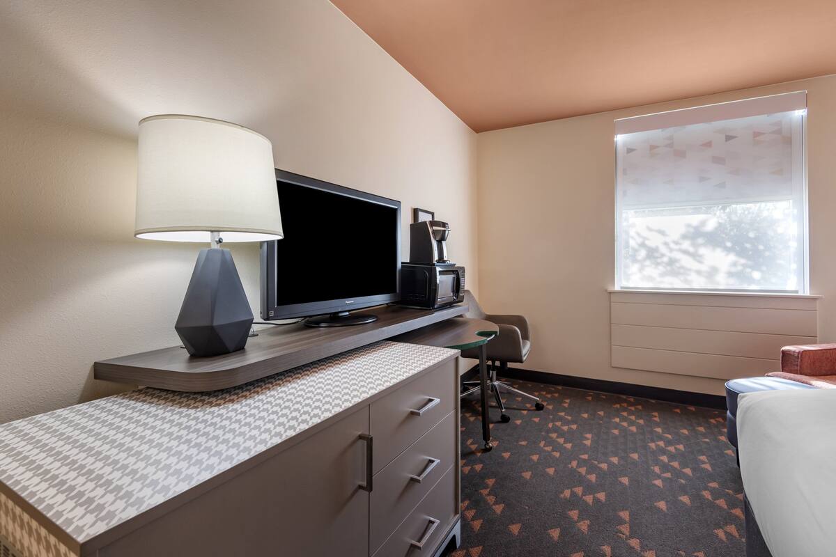 A hotel room with a desk, a television, a coffee maker, a chair, and a bed.