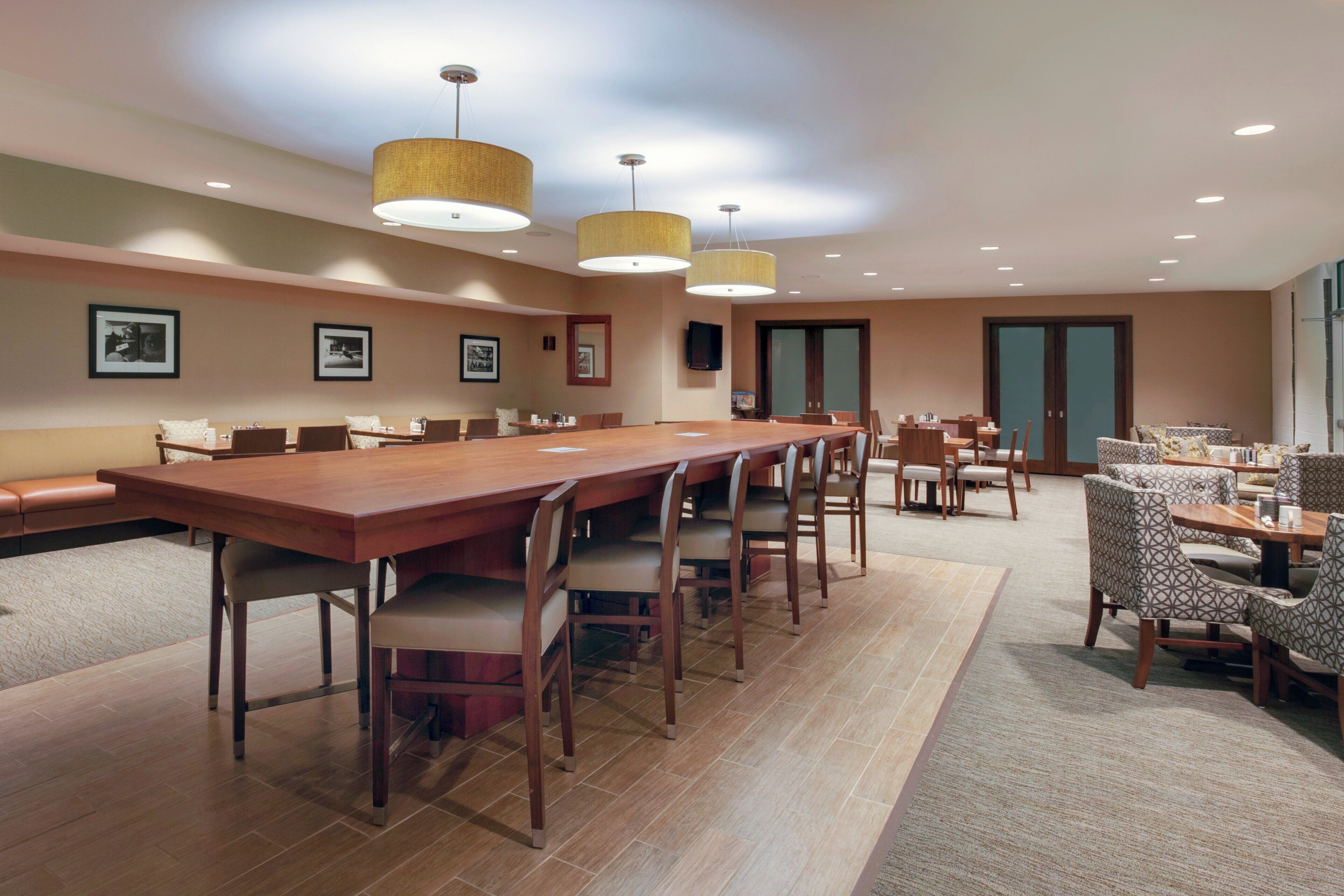 A conference room with a long wooden table, multiple chairs, and pendant lighting.