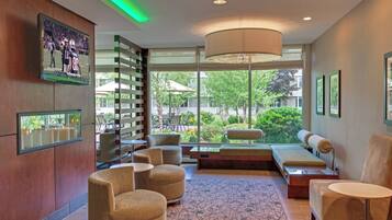 A modern lobby with seating, a large window, and a television displaying a sports event.