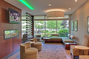 A modern lobby with seating, a large window, and a television displaying a sports event.