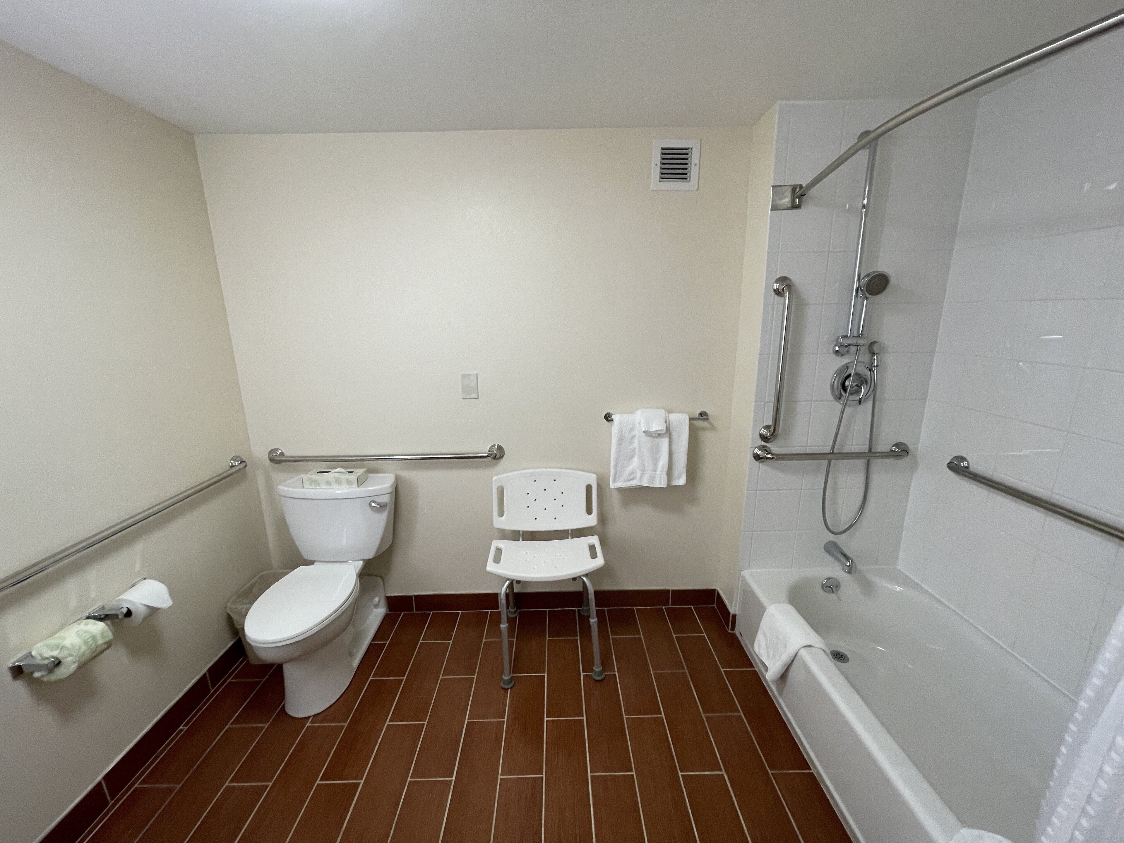 A bathroom with a toilet, a shower with grab bars, a white sink, and a white bathtub.