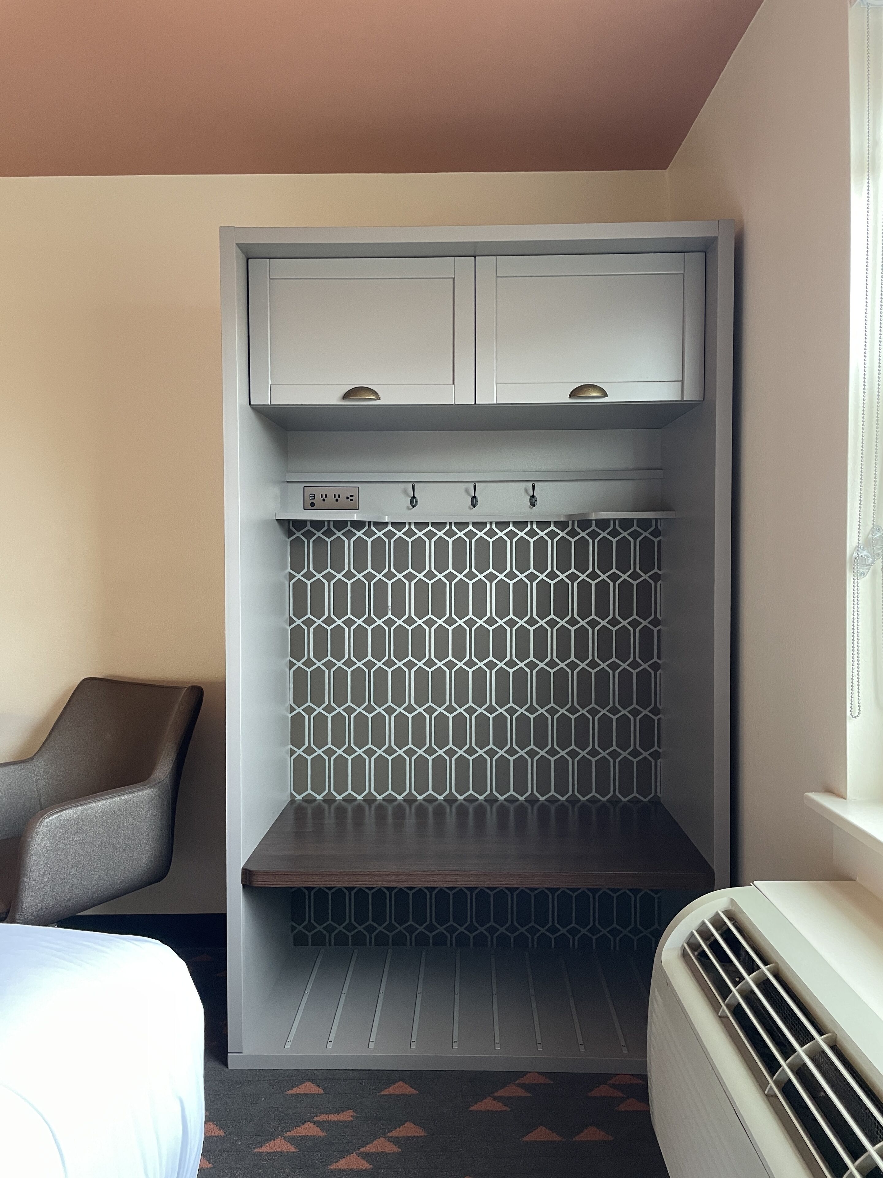 Habitación de hotel con armario empotrado, un frente de azulejos geométricos, un banco y un radiador.
