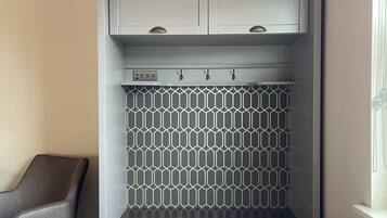 Habitación de hotel con armario empotrado, un frente de azulejos geométricos, un banco y un radiador.