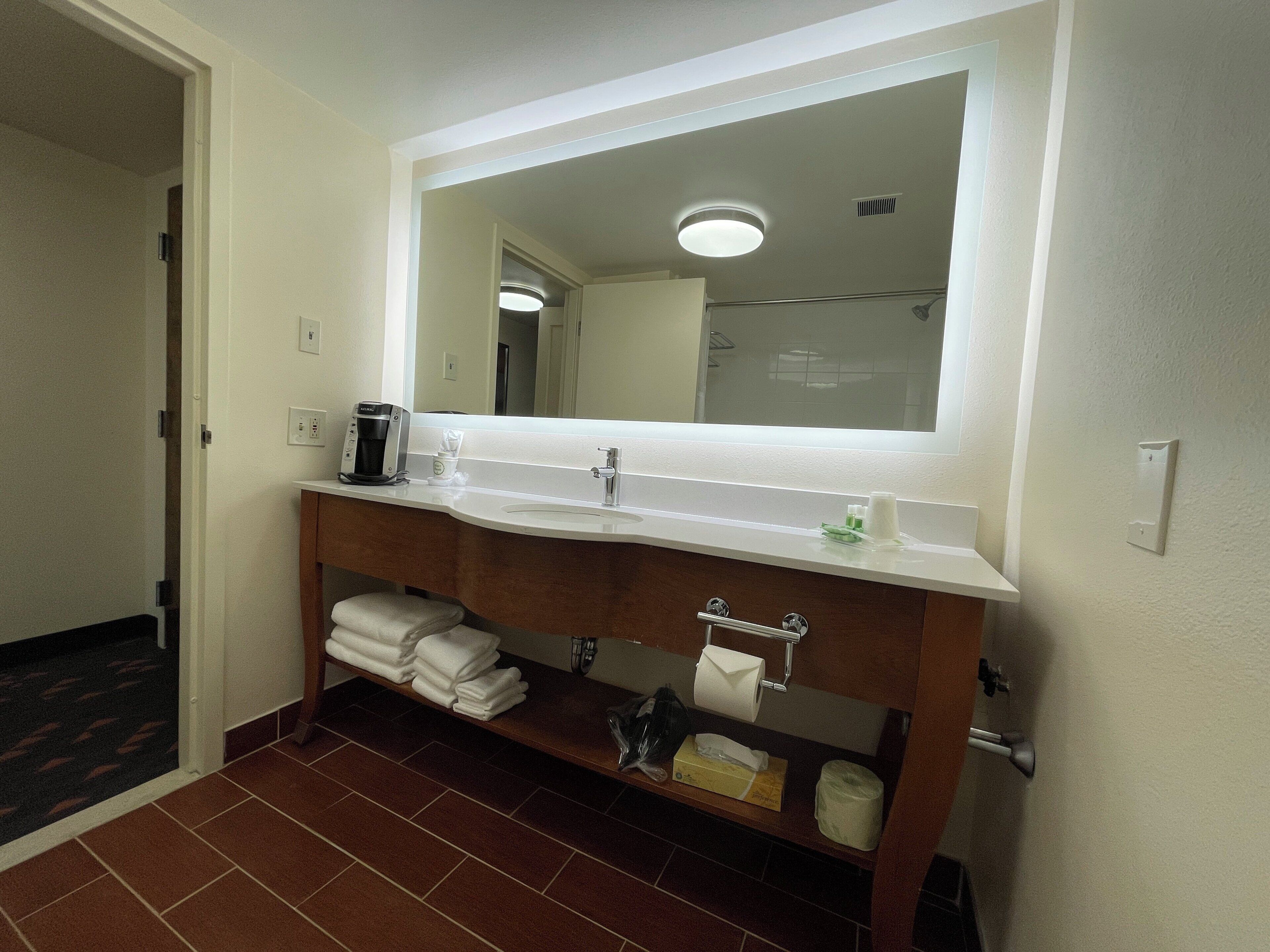 A bathroom with a white sink, a mirror, a towel rack, and a coffee maker.