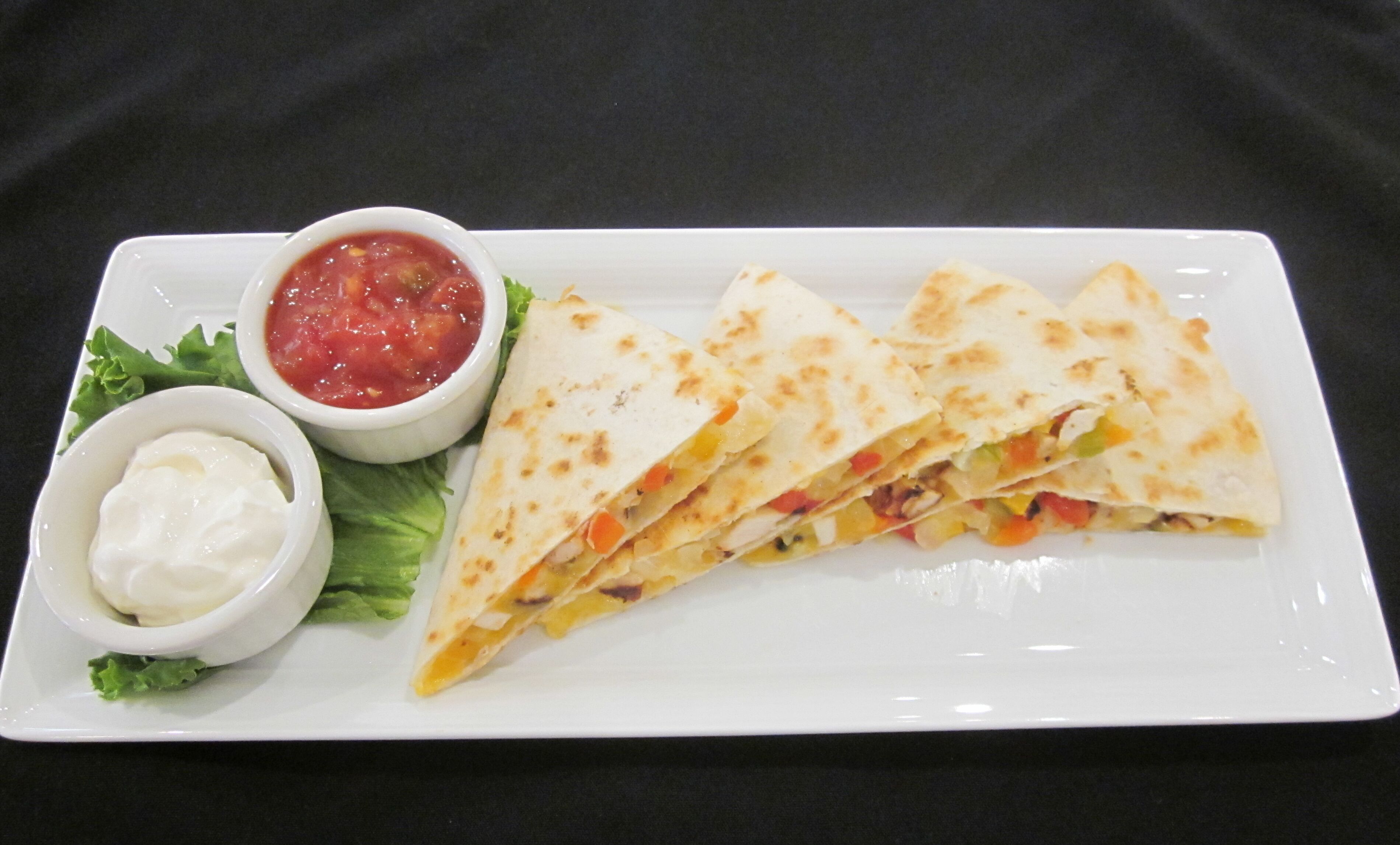 Un plato con tres quesadillas, un tazón de salsa y un recipiente pequeño de crema agria.