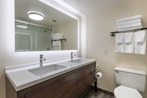A bathroom with a double sink vanity, a toilet, and a glass shower enclosure.