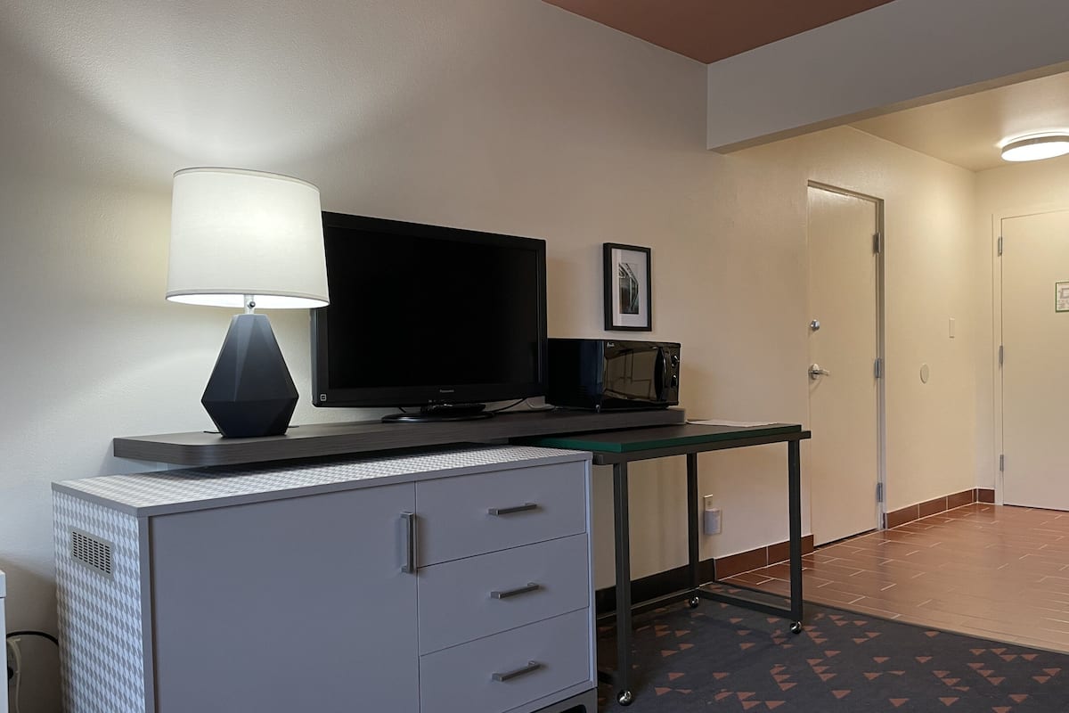 A hotel room with a desk, a flat-screen TV, a microwave, a lamp, and a cabinet.
