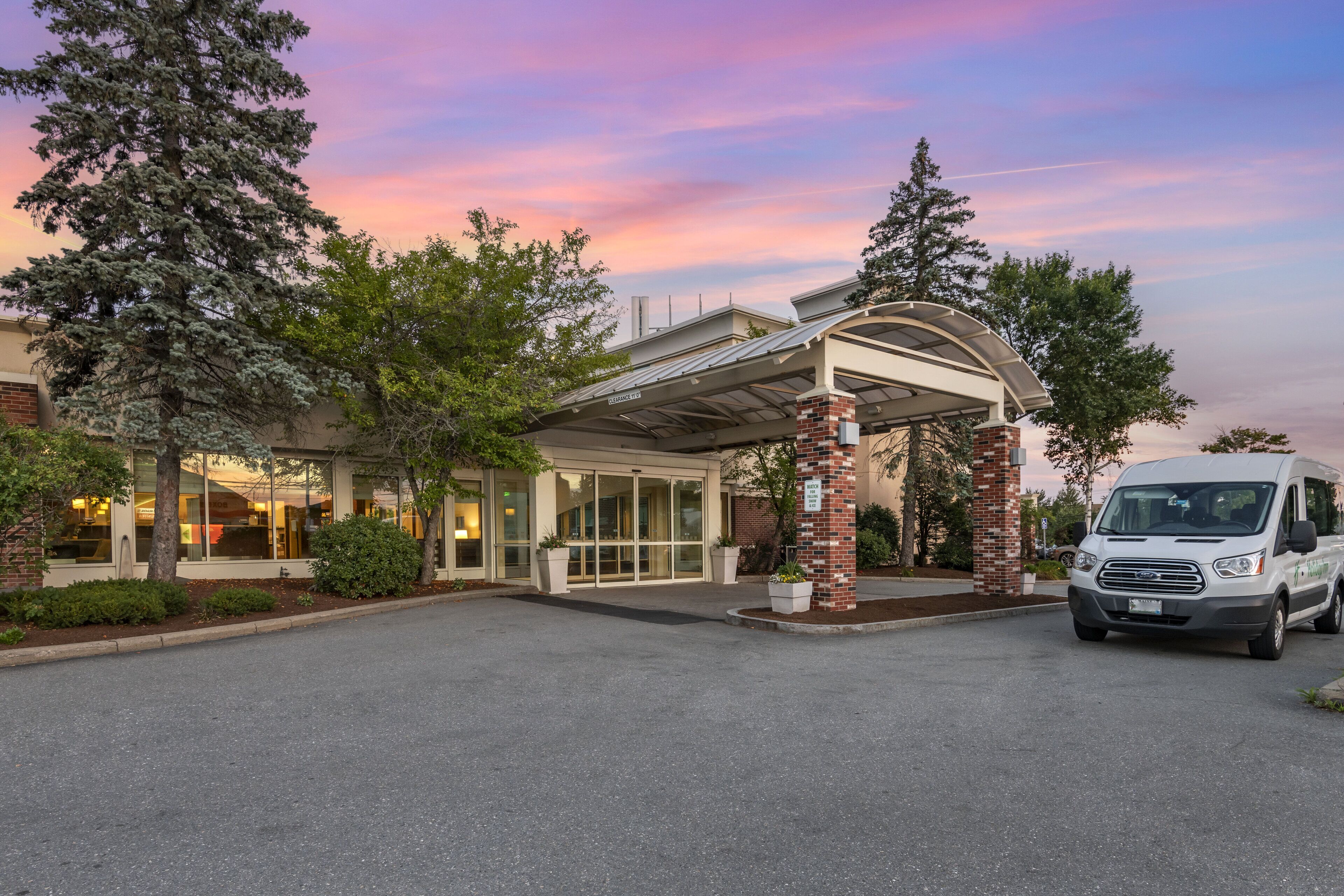 A hotel entrance with a covered driveway, a van parked in front, and a clear sky.