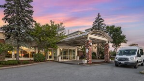 A hotel entrance with a covered driveway, a van parked in front, and a clear sky.