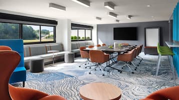 A modern conference room with a large table, comfortable seating, and a large window offering a view of greenery.