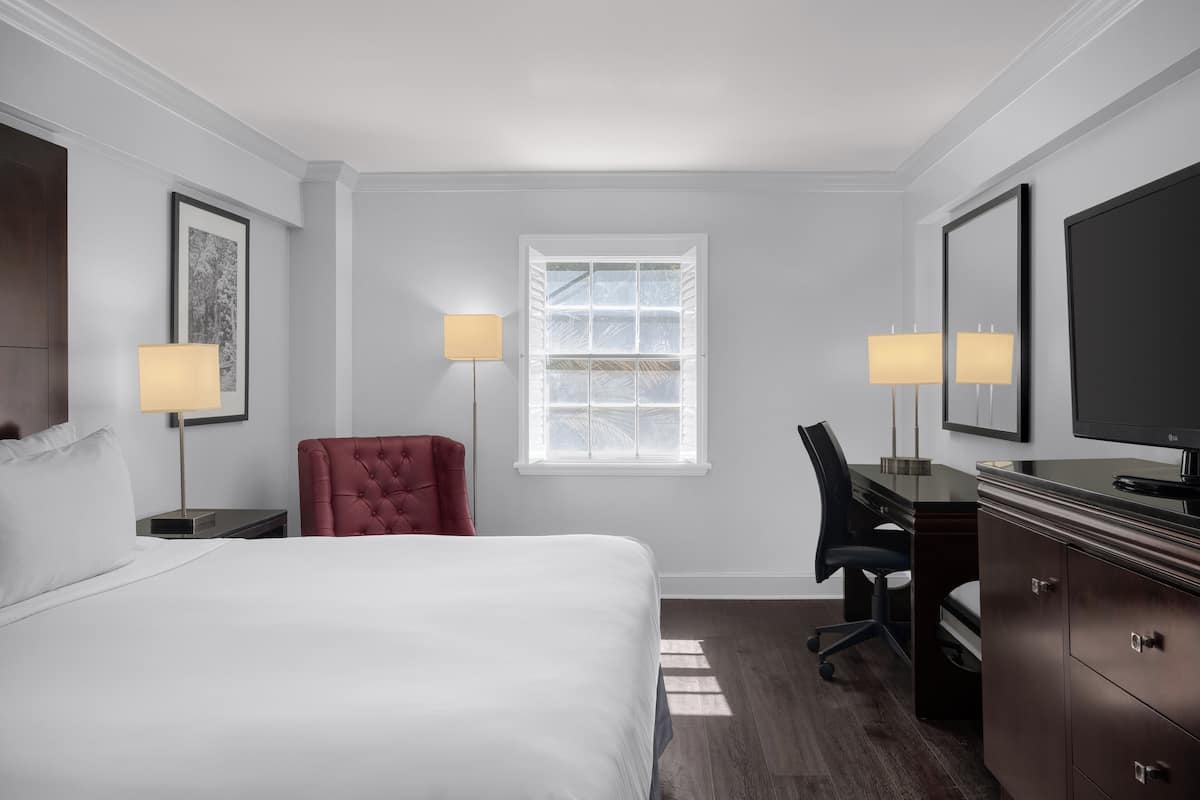 A hotel room with a bed, a desk, a chair, a dresser, and two lamps.