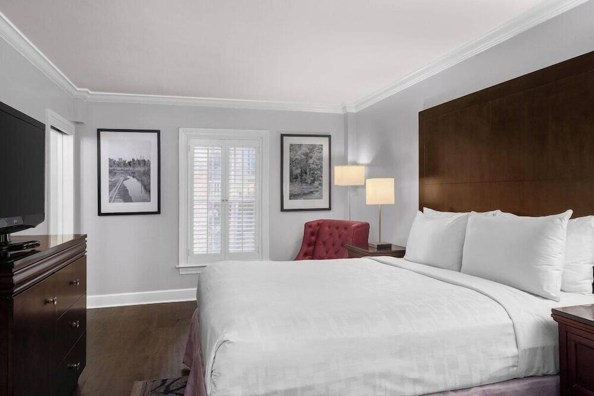 A hotel room with a large bed, a television, a red chair, and framed pictures on the wall.