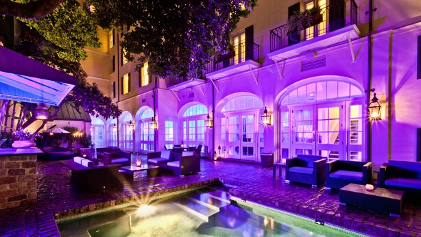 Un’area piscina con posti a sedere e una zona coperta, circondata da un edificio con finestre ad arco e balconi.
